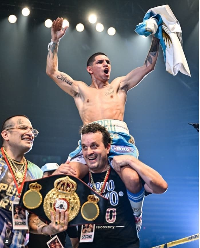 Rodrigo Calabrese carga en hombros a Fernando «Puma» Martínez sobre el ring; Martínez levanta los brazos con una bandera argentina y Calabrese sostiene el cinturón de la Asociación Mundial de Boxeo